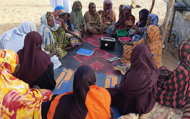 A group of women from a savings group sit in a circle around a lockbox.