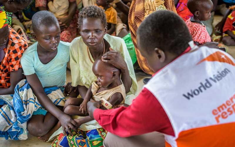An aid worker wearing a World Vision emergency response vest measures the arm of a young child to check for malnutrition.