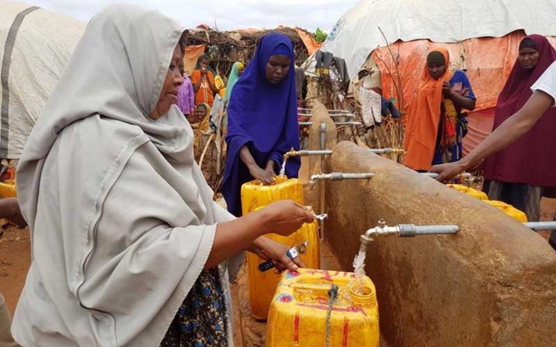 In Somalia, several women gather around borehole taps to fill yellow buckets with water.