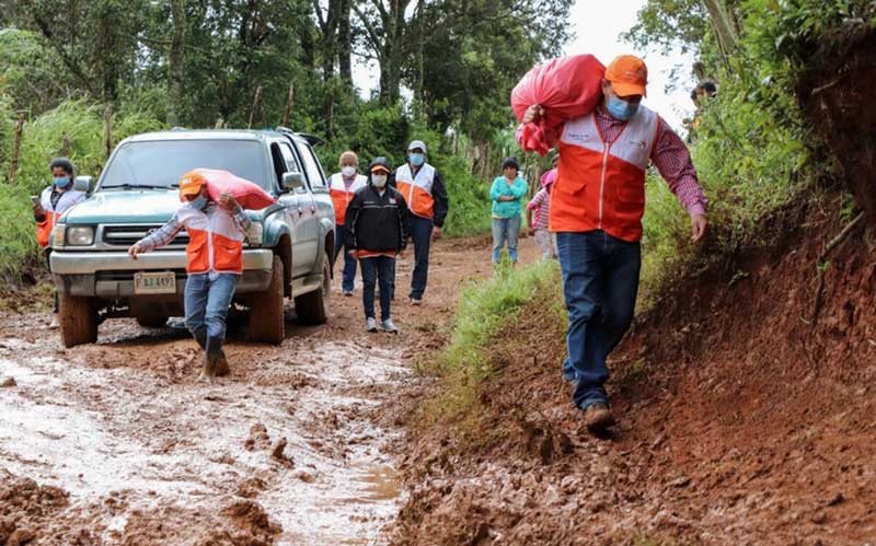 In Honduras, an SUV and workers in World Vision jackets carry emergency supplies along a muddy road.