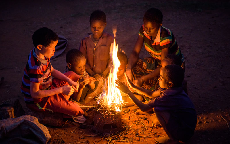 a group of children in Zambia gather around a fire.