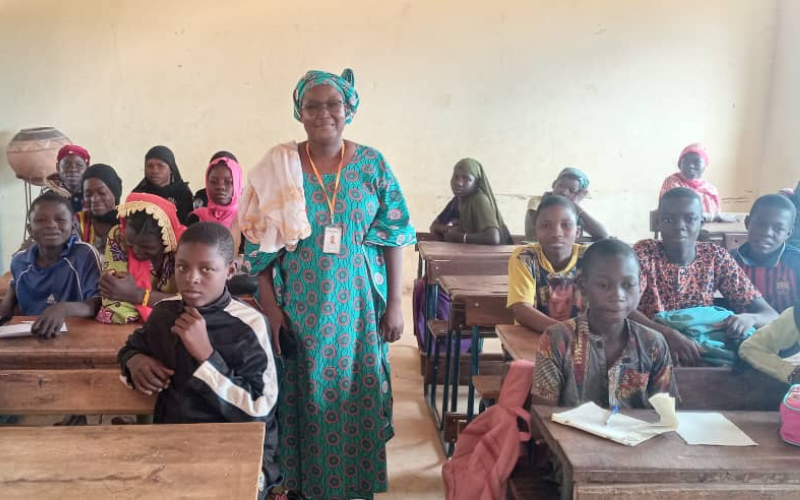 Thérèse stands in a classroom in Mali, with students sitting in desks around her.