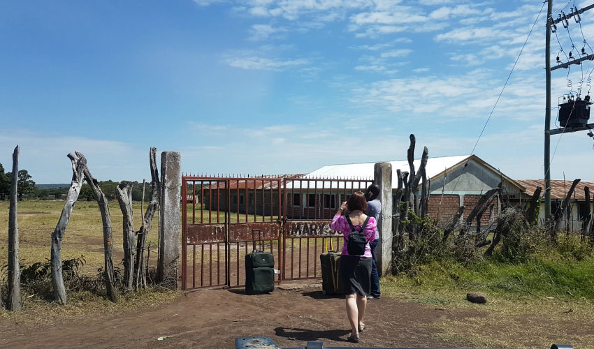 Two people wait in front of a metal gate in a remote location in Kenya