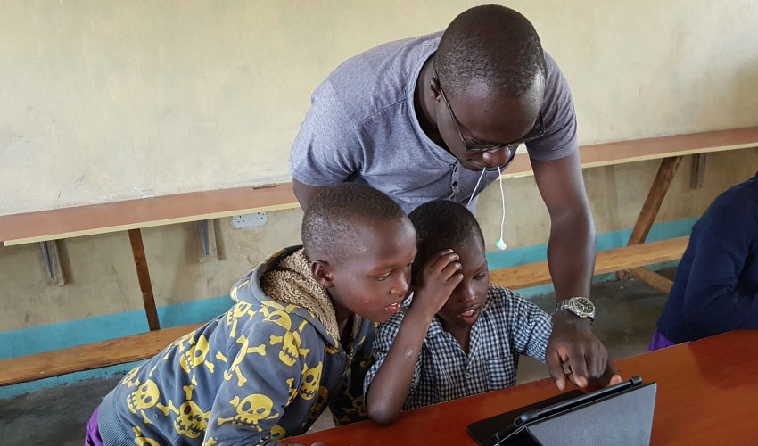 A man helps two students with a tablet literacy activity