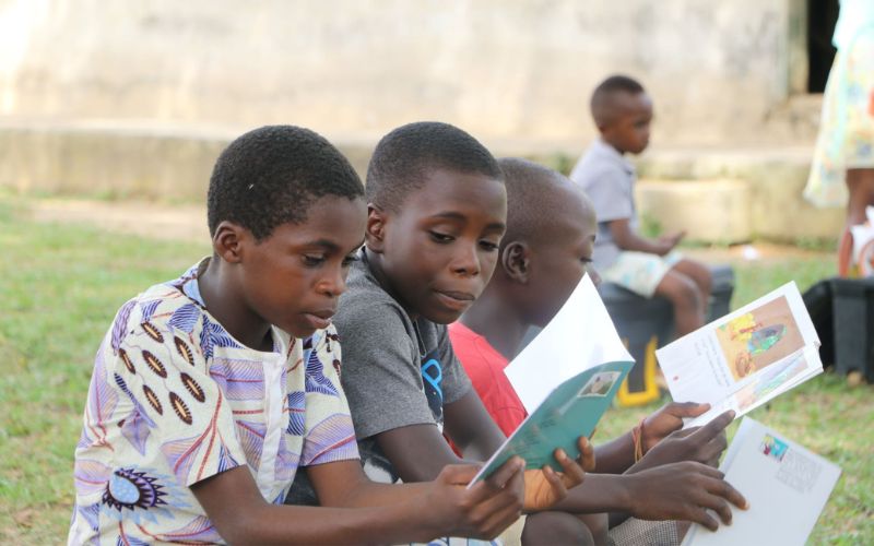 Two Ghanaian boys read books together outside.