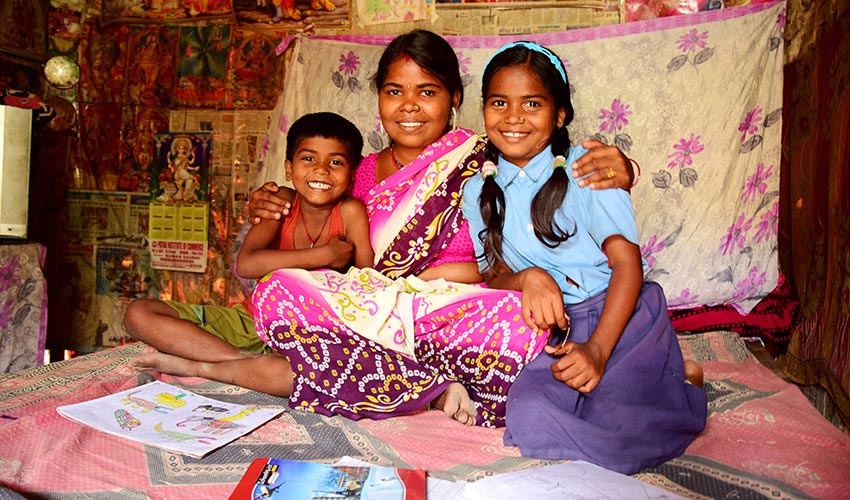 In India, a mother embraces her son and daughter while sitting in their home