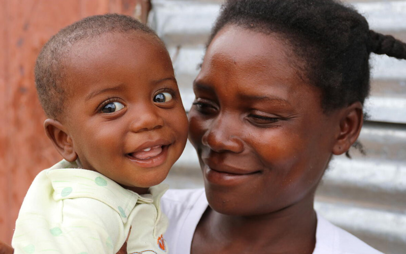 A mother holds a baby boy, who is smiling.