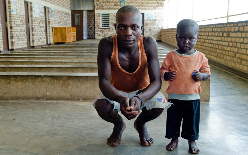 A five-year-old boy stands beside his father, who is squatting beside him.
