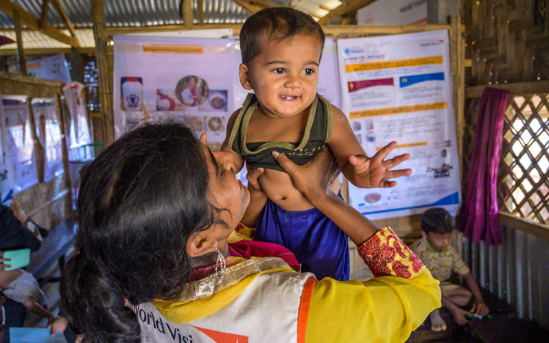 A woman lifts a baby, who is smiling. The woman is wearing a World Vision vest.