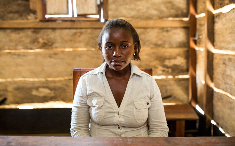 A young girl from Democratic Republic of Congo sits at a desk in a classroom.