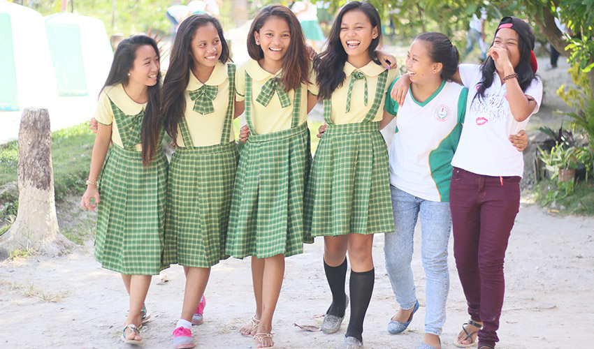 A group of young women, four wearing yellow and green uniforms, with their arms around each other, laughing