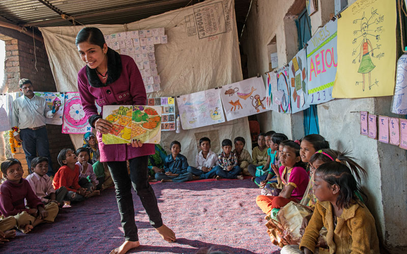 An Indian girl holds a book open to a group of children gathered in a circle