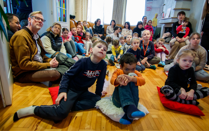 Ukrainian children and a few parents sit together in a crowd on the floor of a house in Moldova.