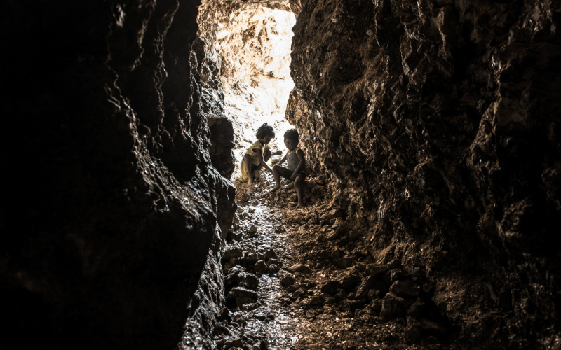 Two small children sit at the mouth of a mica mine.