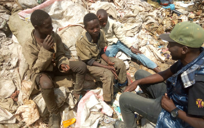 A group of four young men sit on a pile of garbage