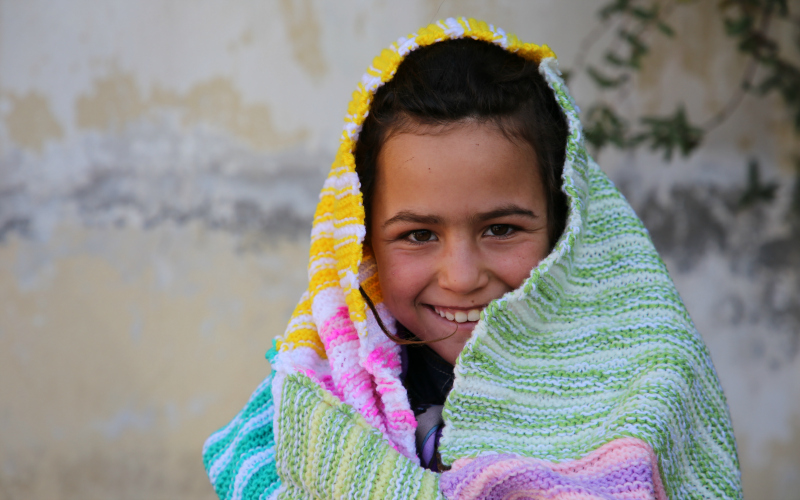 A young girl with a colourful blanket around her smiles