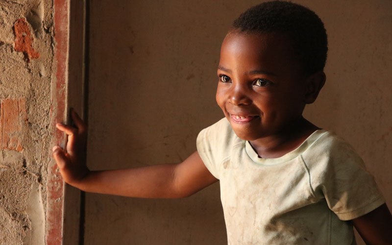a young Zambian girl smiles in a doorway