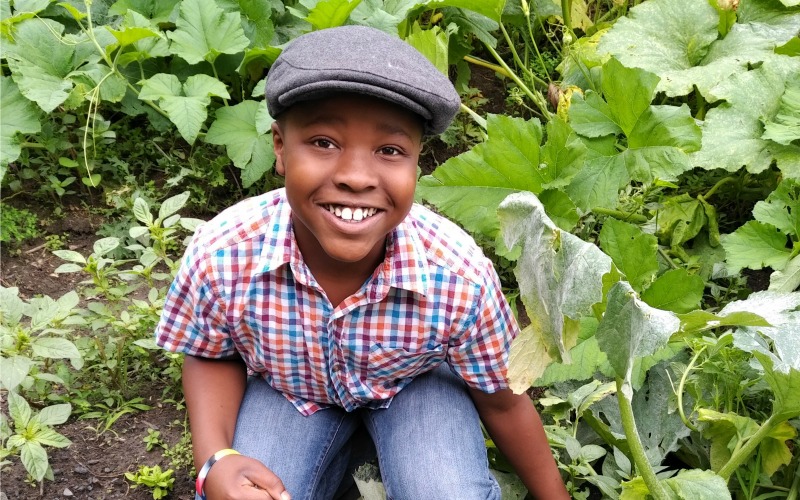A young boy in Canada crouches in his garden
