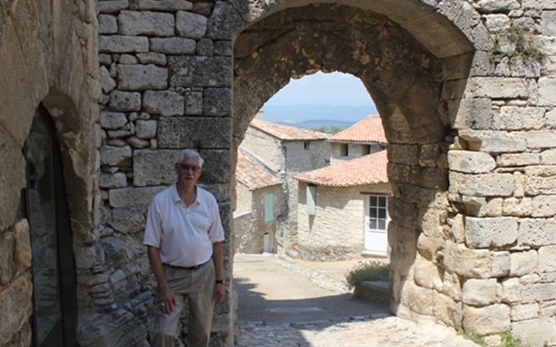 A man standing outside posing under a stone archway.