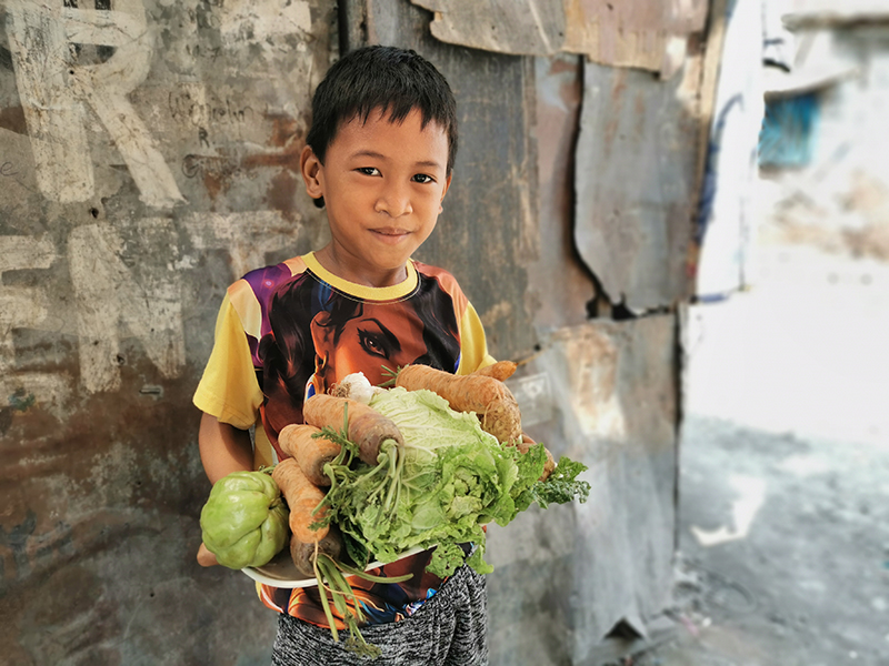 Sponsored child Gero, 8, from the Philippines with a delivery of fresh fruit and vegetables from World Vision.