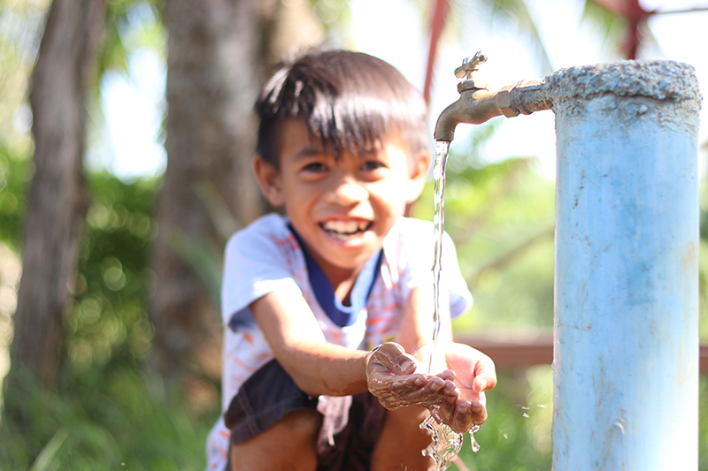 A child from the Philippines washes his hands from a faucet.