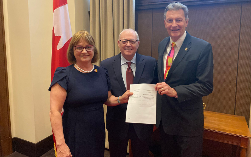 Senator Miville-Dechêne and MP McKay stand together with George Furey, holding the newly passed bill.