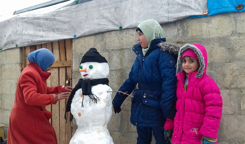 Three girls in winter coats stand around a snowman