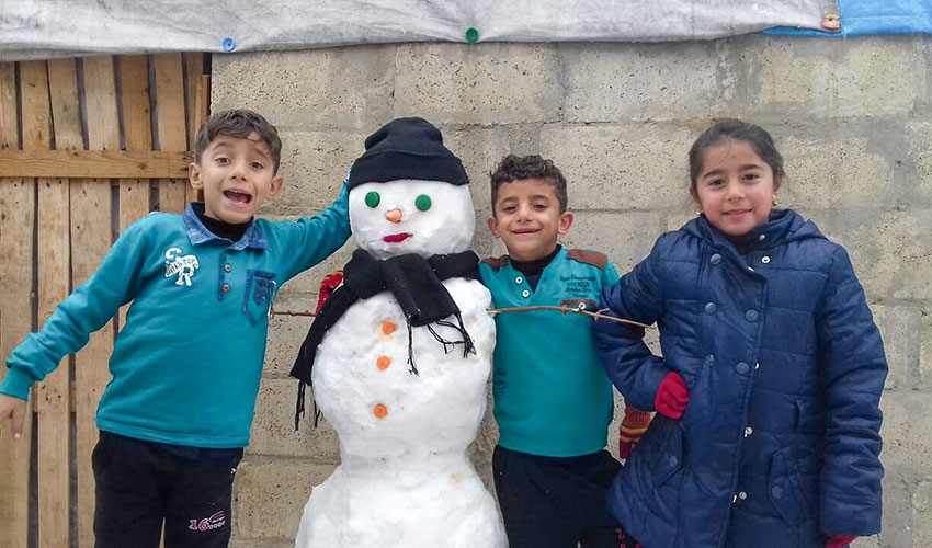 Two boys and a girl smile next to a snowman