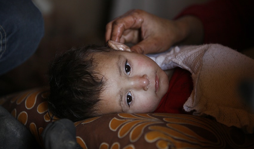 A baby rests her head on a pillow in a Syrian refugee camp, and a relatives strokes her hair.