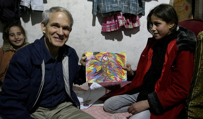 Former President of World Vision Canada, Dave Toycen, sits with children in a room at a refugee camp. One girl shows him a drawing she made.