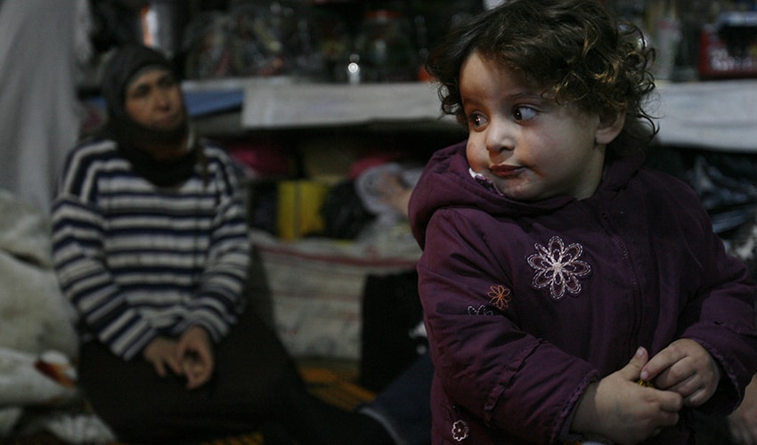 A baby girl living in Syrian refugee camp looks off to the side.