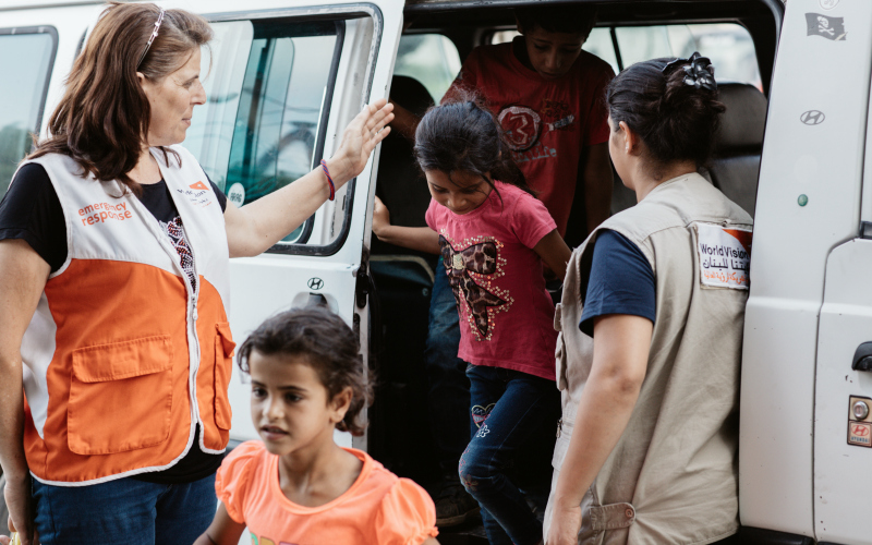 World Vision staff women help Syrian refugee children get off a van.
