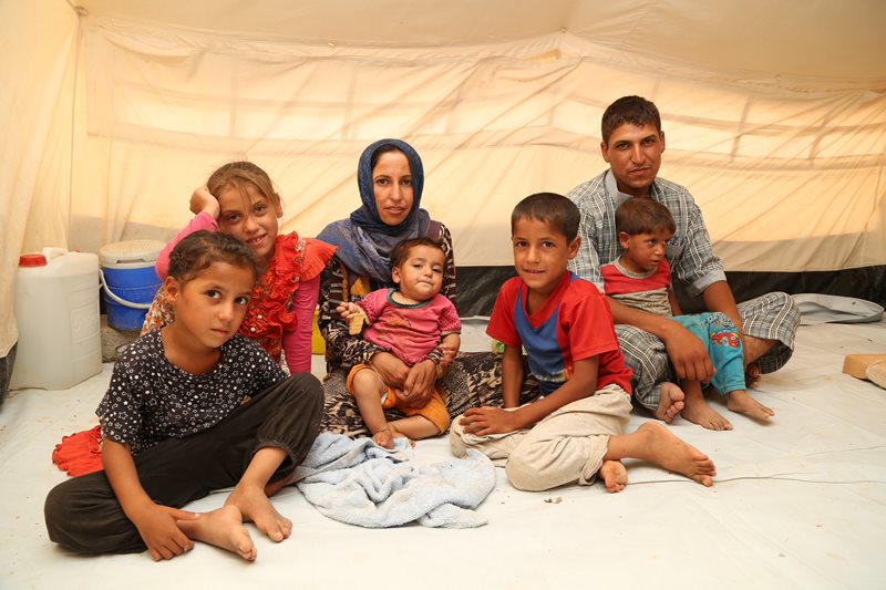 A couple and their five children sit on the floor inside a tent.