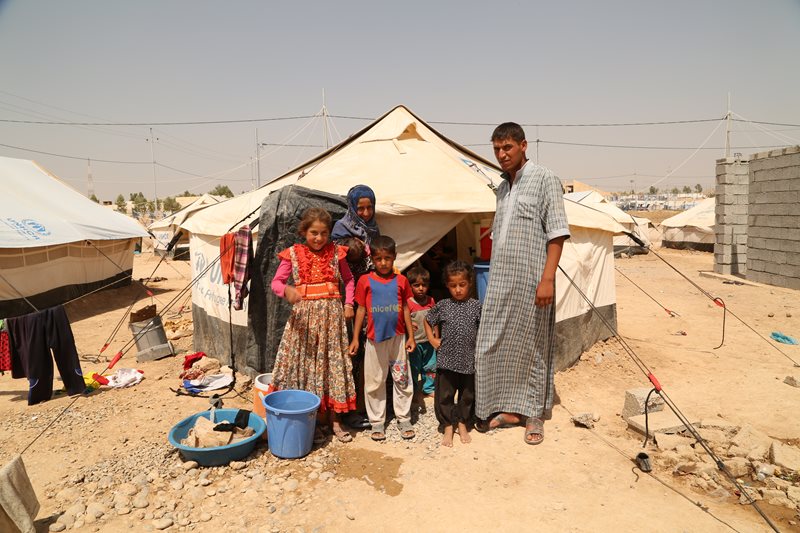 A family of seven stand outside their tent in a refugee camp.