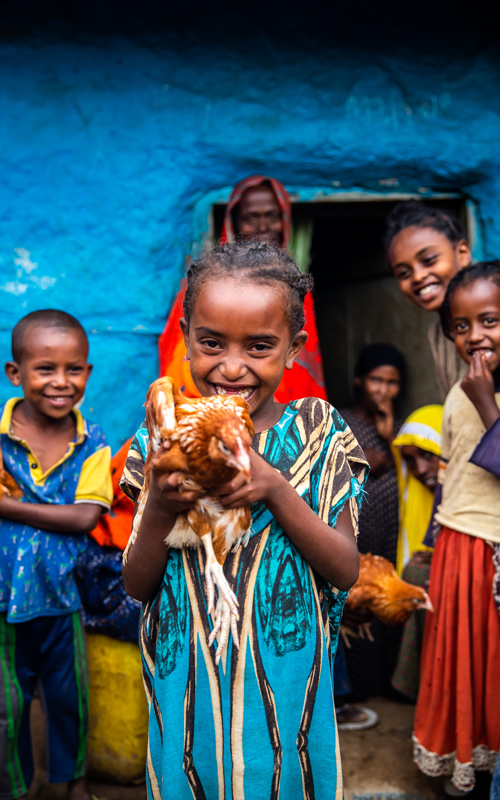 a little Ethiopian girl smiles and holds a chicken up to the camera.