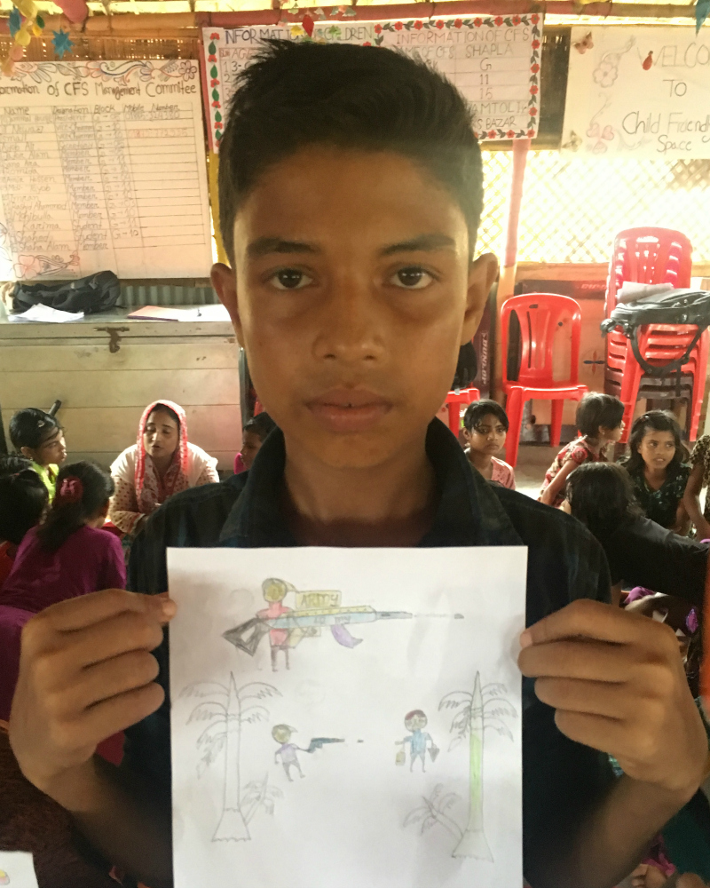 A Rohingya boy holds up a drawing of the violence he encountered in Myanmar
