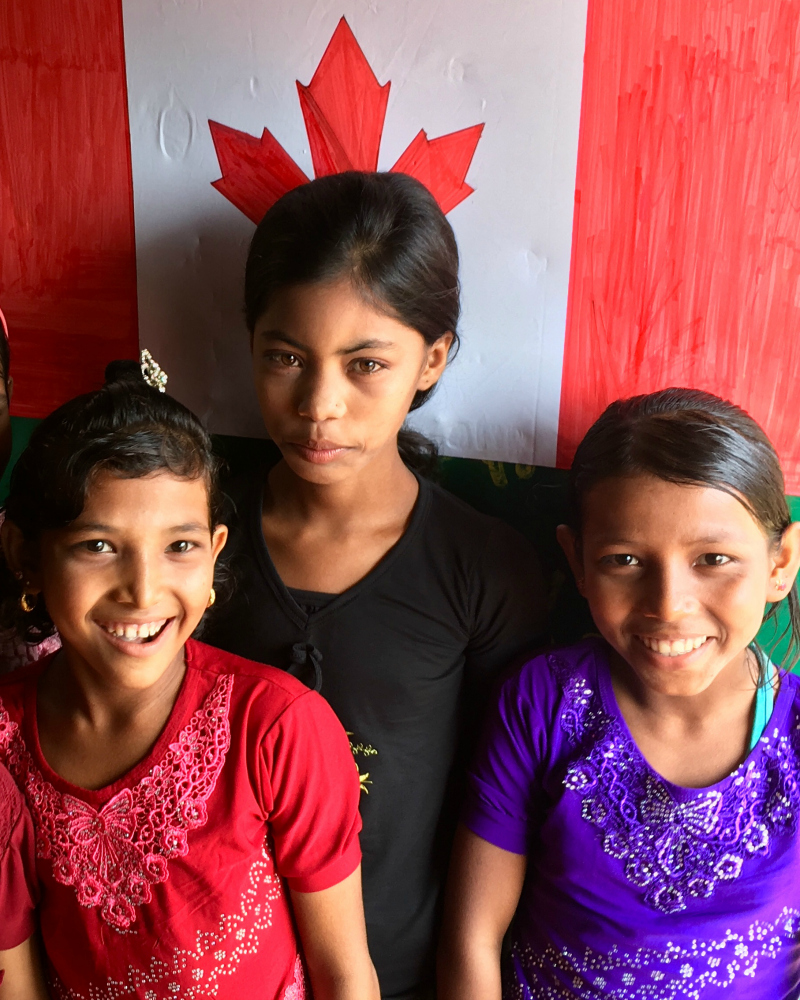 A group of Rohingya girls in front of a Canadian flag