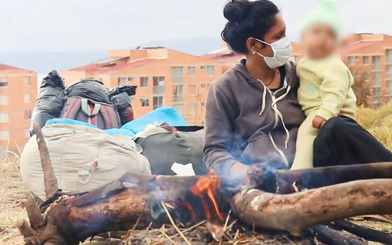 A Venezuelan woman sits by a fire and holds a baby.