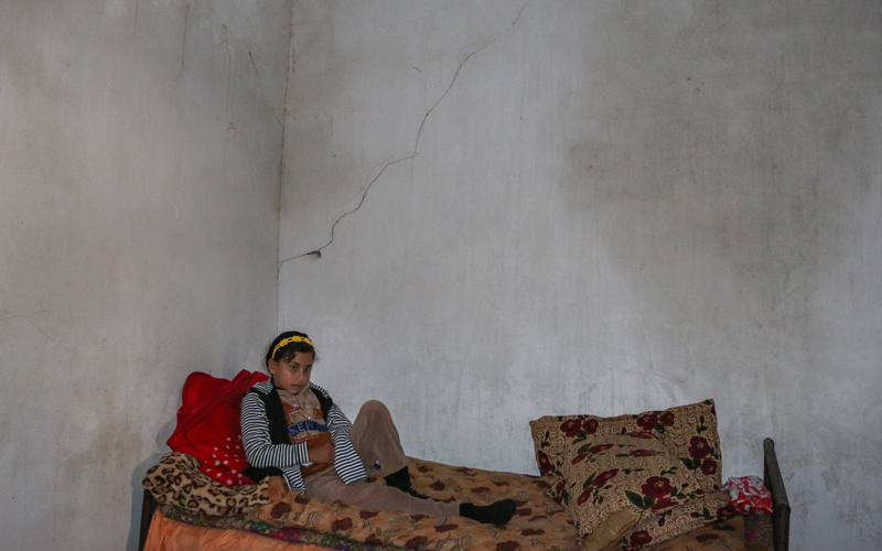 a young girl sits on a bed in a concrete room