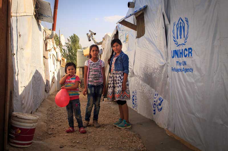 Three Syrian refugee girls stand in front of their tent in the Bekaa Valley region