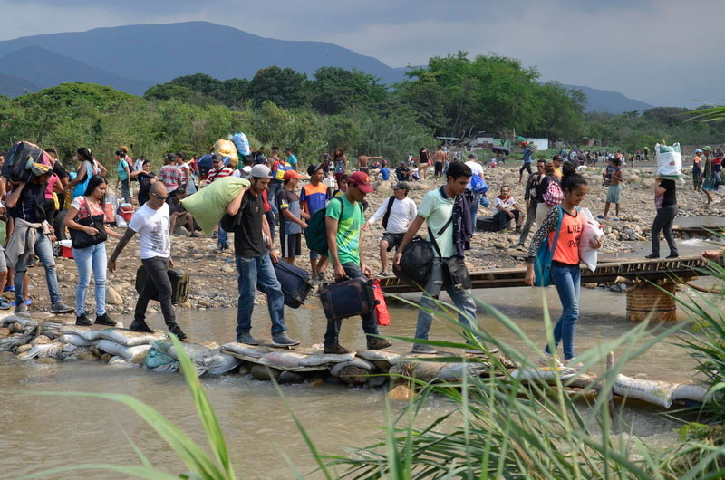 Dozens of Venezuelans carrying their belongings cross a river