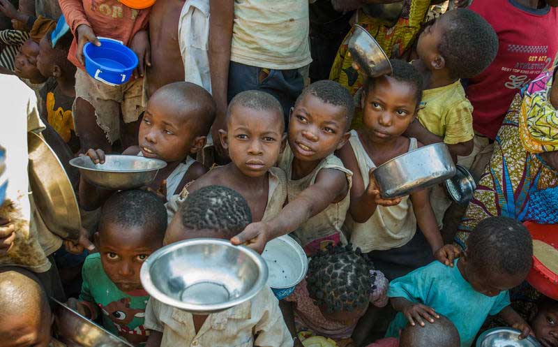 Numerous young children hold up silver bowls to receive porridge at a child-friendly space in the Democratic Republic of Congo