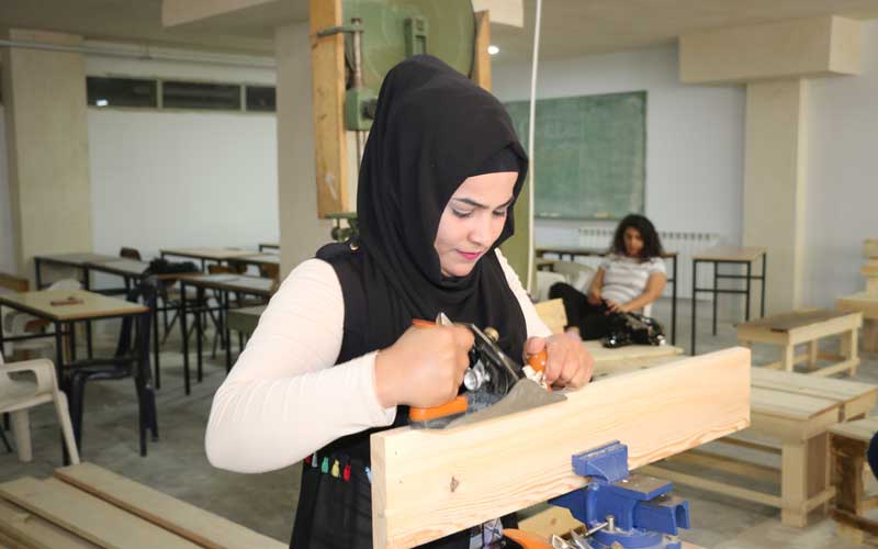 A female student learns carpentry using a machine.