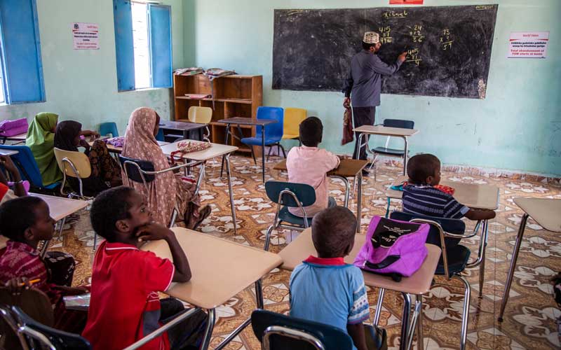 A male teacher stands in front of a class, teaching mathematics to pupils.