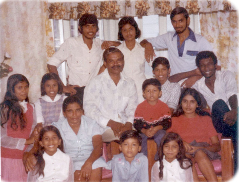 A family portrait photograph from the late 1970s of a large Guyanese family sitting in a living room.
