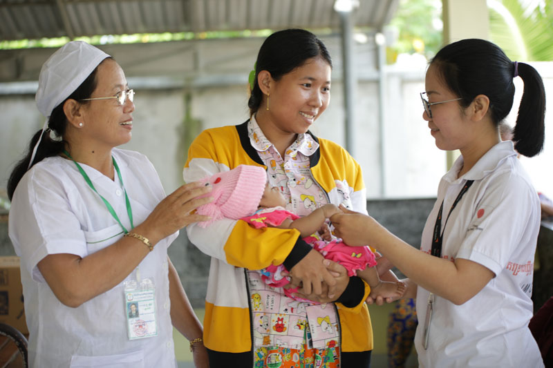 A mother holding her baby receives care from health workers.