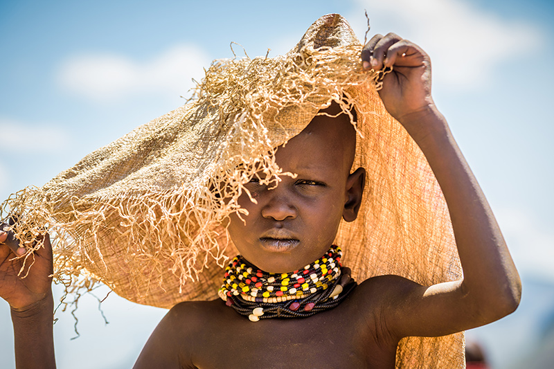 A girl shades herself from the sun with a bag used to carry food from distribution.