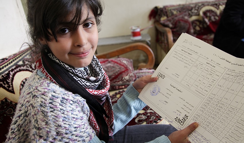 A child who fled the war in Syria holds her last report card.
