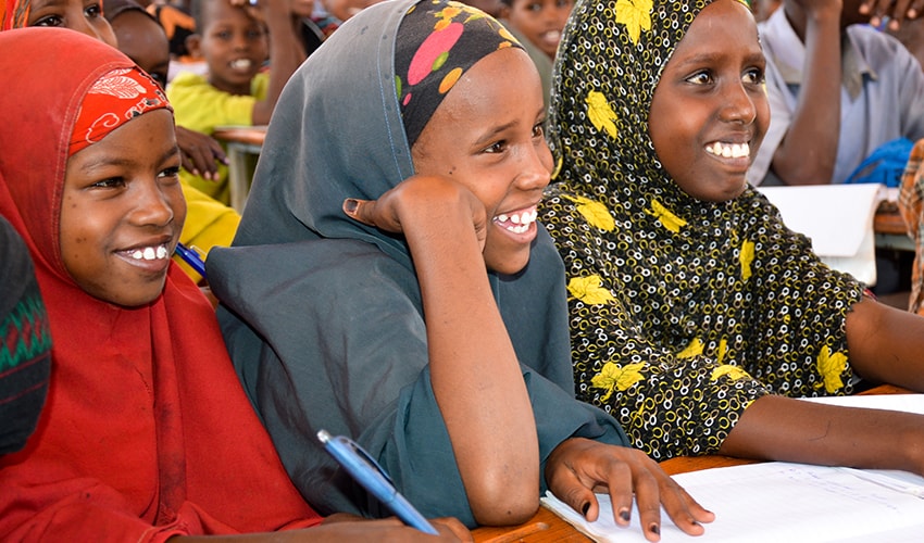 In Somalia, three girls sit in a World Vision learning centre with other students, and they are all smiling.