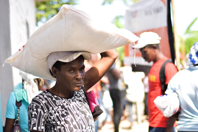 A man carrying a white sack of rice on his head.